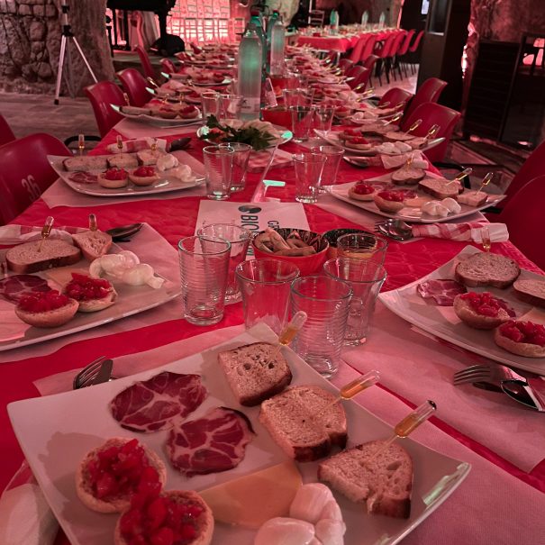 Tavolata presso frantoio rosso ipogeo con una luce soffusa rossa, prodotti tipici della valle d'itria tra cui: pane tipico condito con olio , capocollo di martina franca, mozzarella e formaggi, bruschette